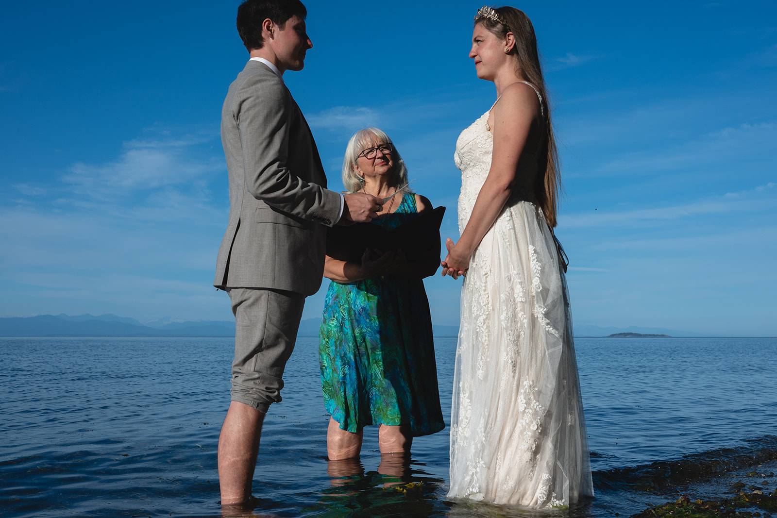 A couple exchanging vows in the ocean shallows under a wide blue sky